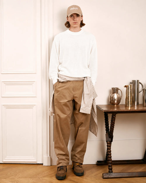homme portant une casquette beige un pull blanc et un pantalon large beige meus paris dans un appartement parisien