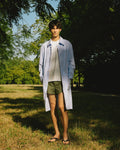 homme portant un manteau léger en coton bleu rayé rouge et un short kaki meus paris dans un bois 