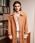 homme portant un manteau terracotta et un ensemble rose meus paris dans un appartement