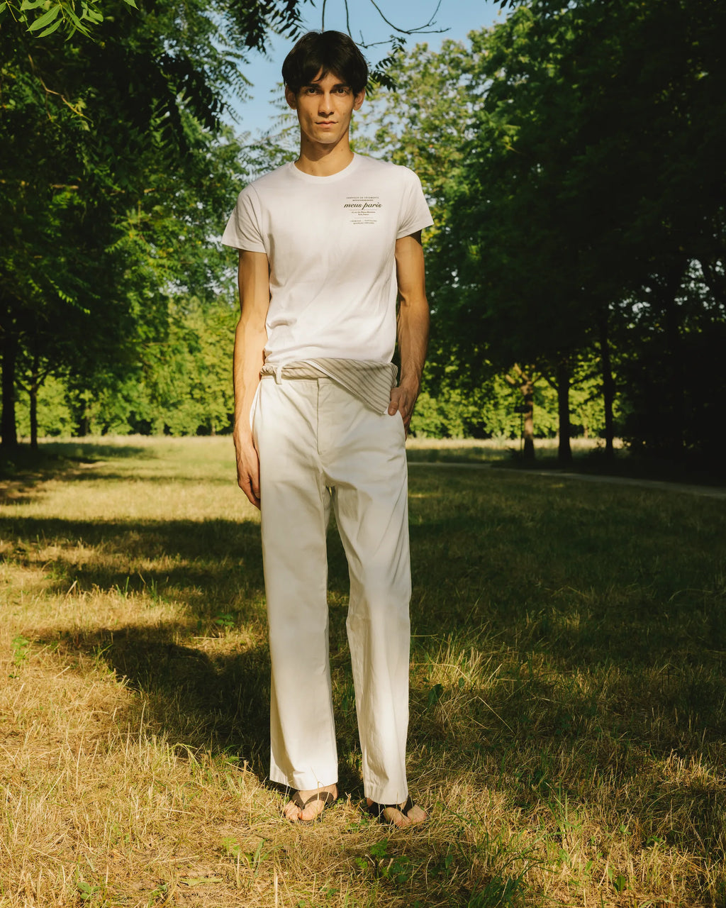 mannequin portant un t-shirt logo meus paris et un pantalon blanc dans un bois 