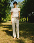 mannequin portant un t-shirt logo meus paris et un pantalon blanc dans un bois 